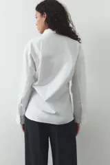 Camisa blanca de cuello solapa y manga larga. Detalle de pliegues con botones. Cierre frontal con botones.