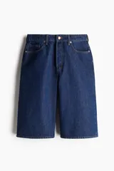 Bermuda de denim azul oscuro, tiro alto, corte ancho, largo a la rodilla y cinco bolsillos. Cierre frontal con botón.