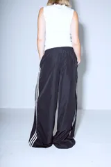 Pantalón Adidas Parachute negro de corte holgado con las tres rayas blancas a los costados.