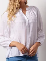 Blusa blanca de gasa bambula marca Zac & Rachel, con cuello a la base y apertura central con botones. Presenta apliques de puntilla en la parte delantera y en las mangas ¾ con terminación fruncida.