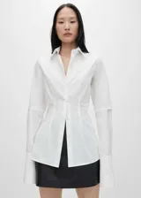 Camisa blanca de algodón con cuello camisero, corte recto, mangas largas con pliegues y puños abotonados.