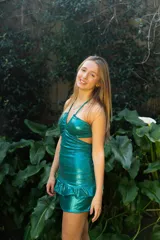 Vestido corto de color verde agua con terminación metalizada, escote halter con tiras finas, corte en la cintura y espalda descubierta. Falda con volados en el ruedo.