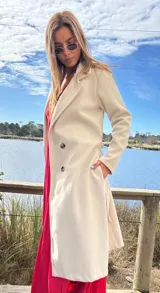 Abrigo trench color crudo, de paño fino con dibujo en sarga, forrado, con cuello solapa, doble botonadura y cinturón con lazada.
