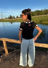 Remera negra de algodón con cuello redondo y mangas cortas. Presenta flores de crochet en tonos beige y blanco en el contorno del cuello y las mangas.