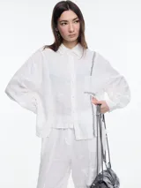 Camisa blanca de lino con calce relajado y diseño asimétrico. Presenta un bolsillo delantero invertido y bordado tipo pespunte en color contraste en el frente y el bolsillo.