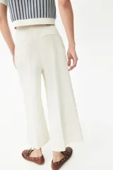 Pantalón palazzo color blanco hueso de tiro alto con elástico oculto en la cintura, cierre lateral oculto y pinzas que realzan la figura. Modelo de corte holgado con bolsillos al bies, bolsillos decorativos atrás y piernas tres cuartos con raya adelante y atrás.