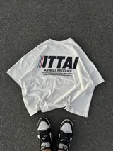 Remera color crema de corte recto y mangas cortas, con estampado en la espalda con el logo "ITTAI" en negro con líneas rojas, azules y blancas, y la leyenda "AN IBIZA PRODUCE. Ittai Stars Department Gallery - Ibiza Edition. If you're in Ibiza, 112 is not an option.".