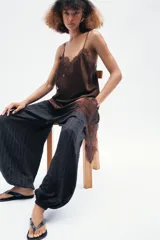 Vestido corto de satén color blanco, con tirantes finos, escote en pico y bajo asimétrico con abertura. Detalle de encaje negro en escote y ruedo.