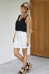 Minifalda blanca de denim con pespuntes negros contrastantes, tiro medio-alto y bolsillos frontales.
