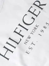 Remera blanca de manga larga con cuello redondo y logo de Tommy Hilfiger estampado en el pecho.