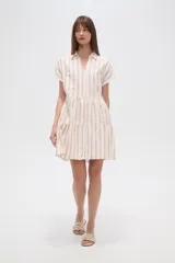 Vestido corto con cuello camisero, de corte holgado y mangas cortas. Presenta un diseño a rayas verticales en tonos beige y blanco, con volados en la falda y cierre frontal con botones.