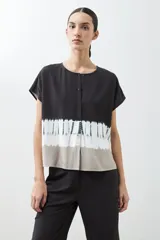 Blusa de manga corta con cuello redondo y cierre frontal parcial con botones. Presenta un diseño tie dye en tonos grises y blancos en la parte inferior.