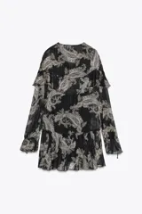 Vestido corto negro con estampado paisley en tonos beige y detalles dorados. Escote en V con lazos ajustables, mangas largas con puños elásticos y volantes en el mismo tejido en el escote y el ruedo.