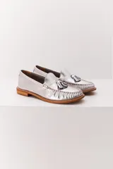 Mocasín de cuero color marrón claro, con detalle de flecos y borlas en la parte delantera. Diseñado en Uruguay y fabricado en Brasil.