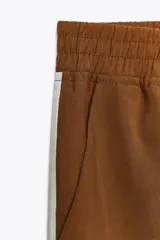 Pantalón marrón de tiro alto con cintura elástica, bolsillos delanteros y detalle de banda lateral blanca a contraste.
