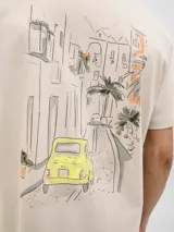 Remera color crema de corte recto y mangas cortas, con cuello redondo. Estampado en la espalda con un dibujo de una calle con edificios, palmeras y un auto amarillo.