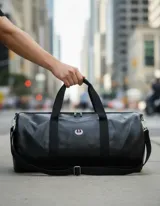 Bolso duffel negro de cuero sintético con logo de ancla bordado en rosa. Tiene doble asa de mano reforzada, correa de hombro regulable y desmontable, cierre superior con doble cremallera y tres bolsillos (dos exteriores y uno interior).