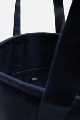 Bolso tipo shopper color azul marino, fabricado en tejido de algodón. Tiene doble asa de mano y un bolsillo plano en el interior.