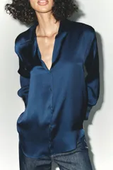 Camisa azul marino de satén con cuello solapa, escote en pico y mangas largas con puños abotonados.
