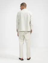Pantalón de vestir color crema, confeccionado en tejido ligero de algodón con textura seersucker. Tiene corte recto, bolsillos laterales y traseros, cierre con botón y cremallera, y parche con logo de la marca.