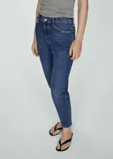 Pantalón de jean azul oscuro, tiro alto, corte mom fit, con cinco bolsillos y cierre de cremallera y botón.