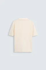 Polo color crema de punto, corte regular fit, con cuello solapa y abertura frontal.
