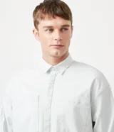 Camisa celeste de algodón, corte oversized, manga larga, cuello camisero, dos bolsillos frontales con solapa y cierre con botones.