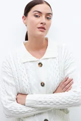 Cardigan crudo de tejido de punto trenzado, con cuello polo, cierre frontal con botones y bolsillos delanteros.