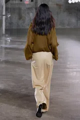 Blusa color marrón con escote en pico, manga larga abullonada con elástico en los puños y volantes en el escote y mangas.