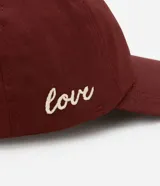 Gorra de sarga color borgoña con bordado de corazón en el frente y la palabra "love" en el lateral.