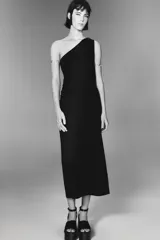 Vestido midi negro de punto, con escote asimétrico, manga sisa y aplique dorado en el hombro.