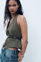 Top de cuello halter color verde oscuro, con escote pico, falso bolsillos de vivo en delantero y cinturón negro con hebilla metálica. Cierre frontal con cremallera oculta.