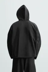 Sudadera con capucha negra, de corte oversize, confeccionada en tejido de algodón con interior en rizo. Cuenta con manga larga, bolsillos frontales tipo canguro, efecto lavado y acabados irregulares con vuelta.