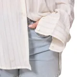 Camisa beige a rayas verticales finas, de corte holgado y mangas largas con puños abotonados.