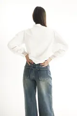 Camisa blanca de estilo romántico con cuello alto, mangas largas abullonadas y detalles de broderie.