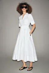 Vestido midi camisero color ladrillo, confeccionado en popelina de algodón. Presenta cuello solapa, manga corta con puños abotonados, bolsillos laterales ocultos y bolsillos de parche con solapa en el pecho. Incluye cinturón lazada en el mismo tejido y cierre frontal con botones ocultos.