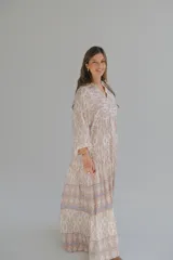 Vestido largo color beige con estampado abstracto en tonos marrones y azules. Tiene cuello mao, mangas largas abullonadas con puños elásticos y falda escalonada.