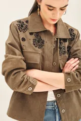 Campera color verde militar con bordados de piedras negras en el canesú delantero y trasero. Tiene bolsillos con solapa en el pecho, jareta ajustable en la cintura y cierre frontal con botones.