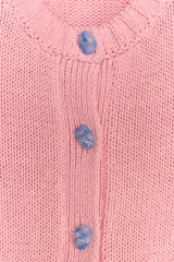Chaqueta de punto rosa con cuello redondo y manga larga. Tiene bolsillos delanteros y cierre frontal con botones celestes.