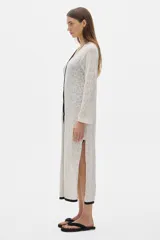 Túnica tipo vestido color crudo, tejido calado, largo midi y cortes a los lados. Tiene cuello redondo y mangas largas.