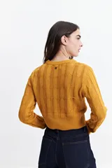 Sweater de punto color mostaza, con diseño de ochos y textura calada. Tiene cuello redondo, mangas largas y terminaciones acanaladas en puños y cintura.