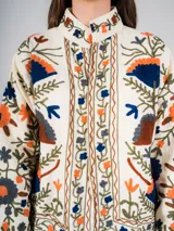 Chaqueta corta color crema con bordados de flores en tonos naranja, azul y verde.