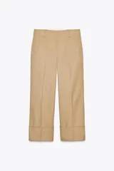 Pantalón color beige de corte ancho, con tiro medio, trabillas en la cintura y raya planchada.