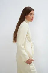 Chaqueta corta color beige, entallada, con escote en V, manga larga y cierre frontal con lazo fijo. Confeccionada en lana fina sin teñir, con bolsillos escondidos y terminaciones enviadas. Hecha 100% en Uruguay.