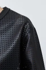 Chaqueta negra de eco cuero calado, con cuello redondo y cierre frontal con botones a presión.