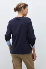 Remera de manga larga color azul marino con cuello redondo. Los puños de las mangas son doblados y revelan un forro de tela a rayas finas blancas y celestes.