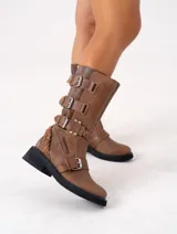 Bota de cuero color marrón con caña media, suela de goma negra, cierre lateral y hebillas ajustables. Presenta detalle trenzado en el talón.