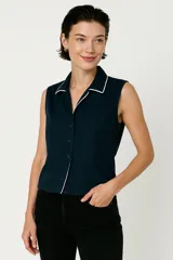 Camisa azul marino sin mangas con cuello clásico, botonadura frontal y vivos blancos en cuello y ruedo. Corte entallado.