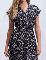Vestido corto estampado blanco y negro, marca Luxology. Escote en V cruzado con solapa, cintura elastizada con pasadores y lazo de ajuste, y manga corta.