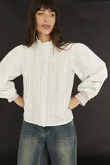 Camisa blanca de estilo romántico con cuello alto, mangas largas abullonadas y detalles de broderie.